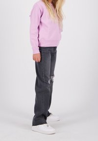 Ljusrosa sweatshirt, grå slitna jeans och vita sneakers. Enkel design, lös passform och mjuk textur. Synliga knäskär på jeansen.