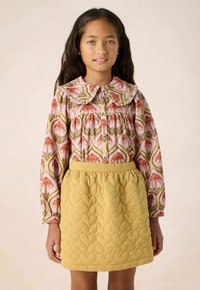 Light pink floral patterned blouse with a ruffled collar, paired with a textured yellow quilted skirt featuring a heart pattern.
