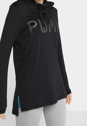 Czarna bluza z kapturem i długim rękawem z dużym, teksturowanym logo "PUMA" na piersi, noszona z jasnoszarymi legginsami, osoba pozująca na białym tle.