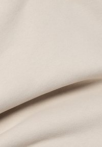 Light beige fabric featuring a soft, textured surface with a smooth finish, folded to showcase its drape and material consistency.