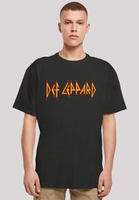 Schwarzes Baumwoll-T-Shirt mit einem auffälligen orange- und gelbfarbenen "Def Leppard"-Logo in einer gezackten Schriftart. Lockere, entspannte Passform mit kurzen Ärmeln.