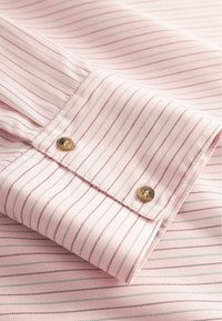 Růžový manžetový límec z bavlny s tenkými modrými a hnědými pruhy. Má dva kulaté knoflíky ve zlaté barvě a hladkou texturu látky.