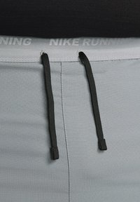 Sive kratke športne hlače iz teksturirane tkanine, z črnimi vrvicami in pasom, na katerem je vtisnjen napis "Nike Running."