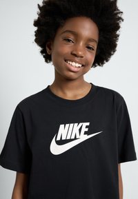 Melnas kokvilnas T-krekls ar izteiksmīgu baltu Nike logotipa grafiku. Ar īsām piedurknēm un apaļu kakla dizainu. Gluda tekstūra.