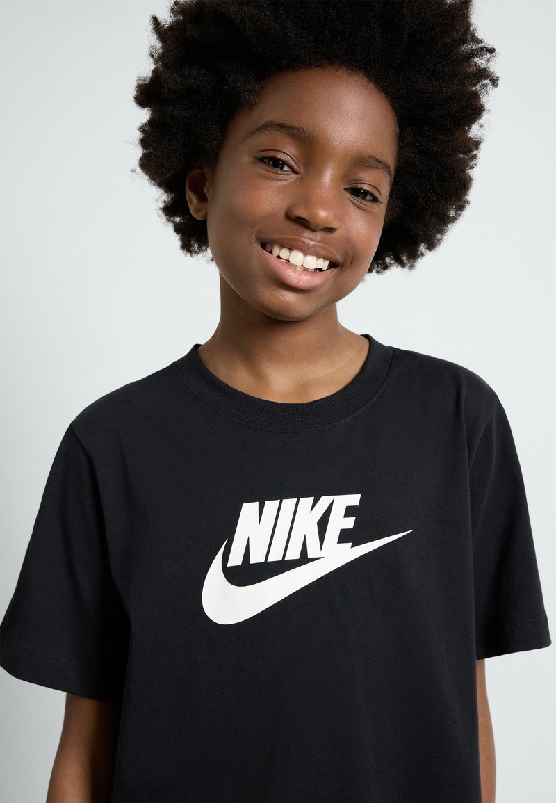 Melnas kokvilnas T-krekls ar izteiksmīgu baltu Nike logotipa grafiku. Ar īsām piedurknēm un apaļu kakla dizainu. Gluda tekstūra.