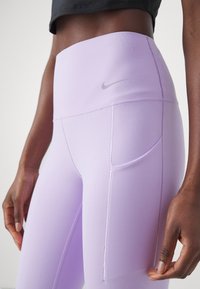 Lichtpaarse high-waisted leggings gemaakt van rekbaar materiaal, met een Nike-logo en zijzak voor opslag. Soepele textuur en aansluitend ontwerp.