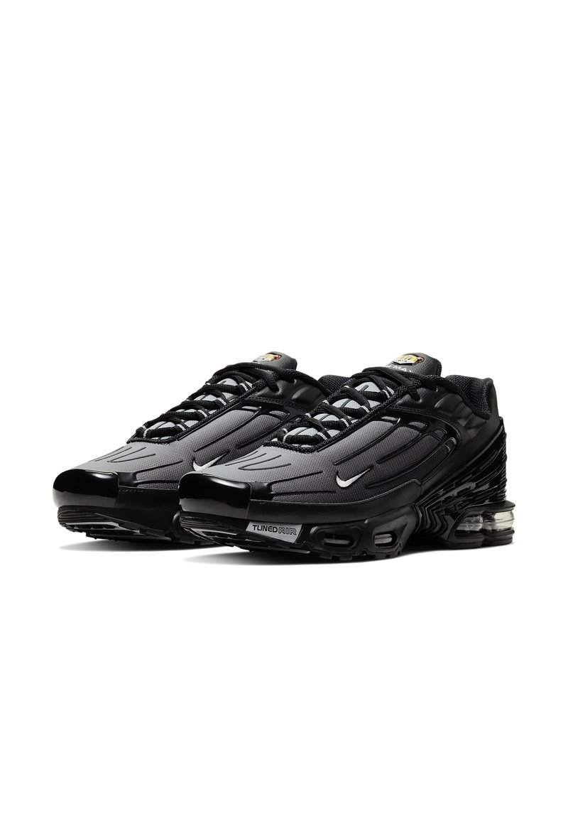 Zapatillas deportivas negras con parte superior de malla texturizada, diseño elegante, acentos reflectantes y una unidad de amortiguación de aire visible en la suela.