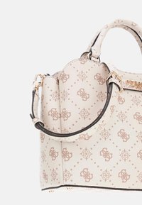 Beige tervezői kézitáska monogrammintával, arany színű fémrészekkel, felső fogantyúval és állítható vállpánttal fehér háttér előtt.
