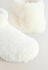 Pehmead, paksud valged pahklaiused saapad ümmarguse varbaga, disainitud sooja ja mugavuse tagamiseks neutraalsel taustal.