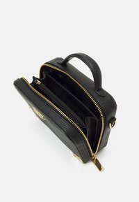 Černá kožená kabelka s texturovaným povrchem, dvojitými zipovými přihrádkami, zlatým kováním a horním uchem. Interiér podšitý černou látkou.