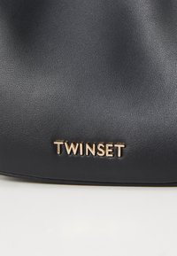 Musta nahkainen käsilaukku, jossa on sileä pinta ja kultainen "TWINESET"-logo. Kompaktin kokoinen, yksinkertainen ja tyylikäs muoto.
