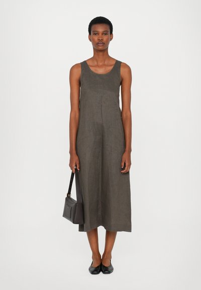 Grå lin ermeløs kjole, kne-lengde, med rund hals. Modellen holder en mørk håndveske og har på seg svarte slip-on sko. Glatt tekstur.
