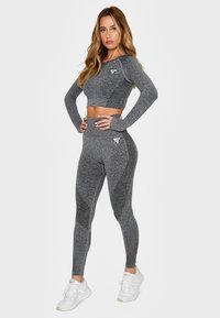 Gray athletic crop top and high-waisted leggings made of textured fabric, featuring a logo on the chest and thigh. Paired with white sneakers.