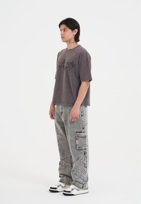 Gray graphic t-shirt with short sleeves, paired with gray cargo pants featuring white embroidered details, and black and white sneakers.