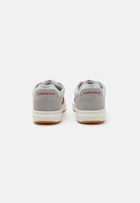 Adidași gri din suede și plasă cu tălpi din cauciuc alb, cu branding roșu Converse pe spate și un guler moale, căptușit.