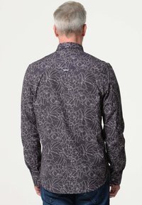 Heren langpoloshirt in donkergrijs met een wit bloemenpatroon, knoopkraag en gebogen rand. Gemaakt van lichtgewicht stof met een gladde textuur.