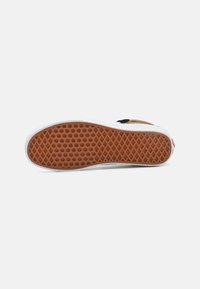 Semelle en caoutchouc brun avec un motif en chevrons texturé, bords blancs et accents noirs. Conception durable pour une bonne adhérence.