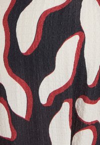 Motivo astratto di tessuto con forme curve in bianco e nero contornate di rosso. Superficie tessurizzata con un aspetto imbottito.