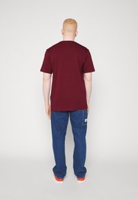 Bordová bavlněná trička s krátkými rukávy kombinovaná s modrými denimovými kalhotami. Tento outfit obsahuje jemný detail loga na džínech.