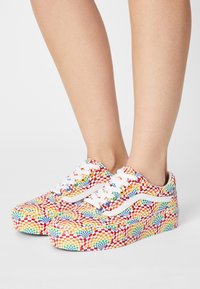 Barevné tenisky s geometrickým vzorem v červené, žluté, zelené a modré barvě. Bílé tkaničky a boční pruh; design platformy.