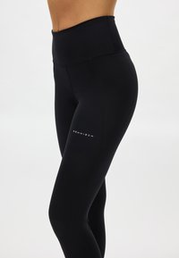 Zwarte legging met hoge taille gemaakt van rekbaar materiaal, met een gladde textuur en een discreet wit logo op de linker dij.