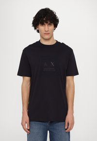 Camiseta de algodón azul marino de manga corta, con un logotipo cuadrado tonal "AX" en el centro, cuello redondo y corte relajado.