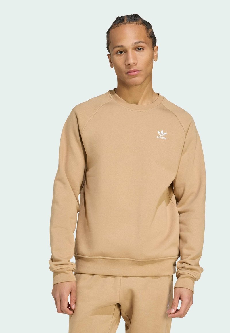 Sudadera beige con puños y dobladillo acanalados, cuello redondo y logo de Adidas en el pecho. Tejido suave y corte relajado.