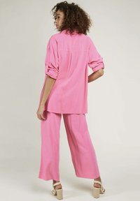 Ensemble deux pièces en tissu rose vif. Chemise décontractée à manches roulées et pantalon large. Matériau texturé, design relax.