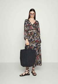 Vestido maxi floral com mangas longas, fundo escuro, várias flores coloridas. Mala tote preta acolchoada, sandálias pretas planas com tiras.