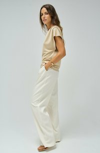 Top beige de manga corta, pantalones anchos blancos y sandalias color tostado. Tejido suave con un ajuste relajado y un detalle mínimo.