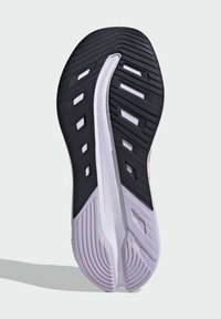 Semelle de chaussure de course en noir et blanc avec un motif de caoutchouc texturé, des rainures pour adhérence, et des accents roses près du talon.