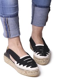 Espadrillas in bianco e nero con suole in paglia intrecciata, dotate di cinture a taglio e punta arrotondata. Sono visibili jeans con cuciture dettagliate.