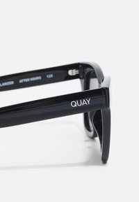 Black sunglasses with a glossy finish, featuring bold rectangular frames. "QUAY" logo is prominently displayed on the side.