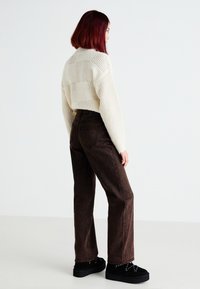 Pulôver de malha creme com padrão texturizado, combinado com jeans castanhos de perna reta e de cintura alta, e sapatos de plataforma pretos. Vista traseira.