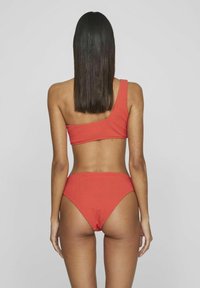 Bikini rojo de un solo tirante con textura acanalada. La parte superior es asimétrica y la parte inferior presenta un diseño de cintura alta.