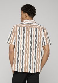 Chemise à manches courtes avec un motif en zigzag dans des tons terreux de brun, blanc et noir. Confectionnée en tissu texturé avec un col et un dos ouvert.