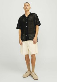 Czarna dziergana koszula z krótkim rękawem o otwartym splocie, białe guziki, w połączeniu z jasnobeżowymi szortami z korduroy i beżowym obuwiem.