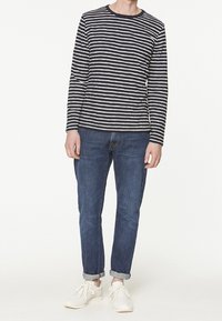 Långärmad marinblå och vit randig skjorta, kombinerad med ljusblå avsmalnande jeans och vita sneakers. Avslappnad, bekväm passform med uppvikta ärmar.