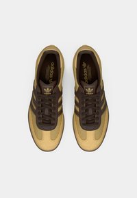 Bruna och gula sneakers med överdel i mesh och mocka, med tre bruna ränder, bruna snören och en guldtags-logotyp på tungan.