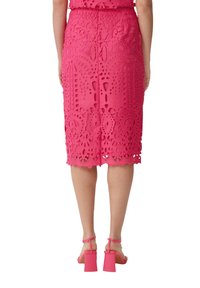 Jupe midi rose avec des motifs en dentelle élaborés, ourlet festonné et silhouette ajustée ; assortie à des sandales à talons carrés.