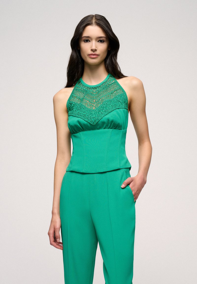 Top verde senza maniche con scollatura in pizzo strutturato e corpetto aderente, abbinato a pantaloni a gamba larga coordinati, che presentano una silhouette pulita.