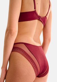 Ensemble de lingerie bourgogne comprenant un soutien-gorge en tissu lisse avec des fines bretelles et une culotte assortie avec des panneaux en tulle et des accents en dentelle.