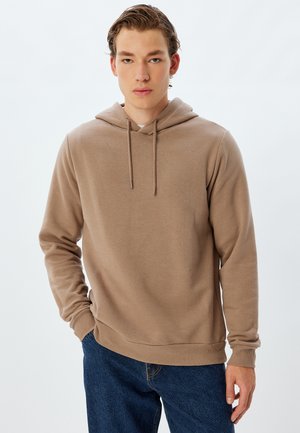 Sudadera marrón con cordón, de mangas largas, puños y dobladillo acanalados, hecha de una suave tela texturizada. Llevada con jeans de mezclilla azul oscuro.