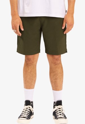 Oliivinvihreät puuvillahousut, joissa on suora leikkaus, polvipituus ja sivutaskut. Yhdistettynä valkoisiin sukkiin ja mustiin korkeisiin tennareihin.