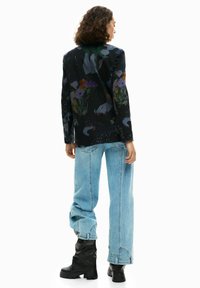 Blazer nero con motivi floreali, caratterizzato da accenti verdi, viola e arancioni. Abbinato a jeans oversized azzurri e stivali neri.