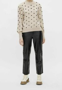 Beige strikket sweater med sorte prikker, rund halsudskæring og puffede ærmer, parret med sorte læderbukser og cremefarvede combat støvler.