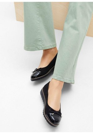 Ballerine nere con una punta in vernice lucida, corpo in suede e un dettaglio a fiocco. Indossate con pantaloni verde chiaro, che mettono in risalto il design arrotondato.