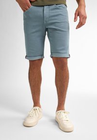 Shorts de denim azul claro con bajos doblados, con bolsillos frontales. Usados con zapatillas de color crema, mostrando un ajuste relajado y un estilo casual.