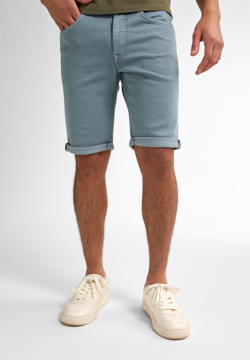 Shorts de denim azul claro con bajos doblados, con bolsillos frontales. Usados con zapatillas de color crema, mostrando un ajuste relajado y un estilo casual.