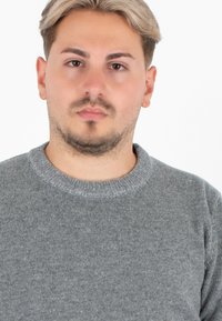 Maglione grigio a maglia con colletto rotondo e bordi a costine. Il tessuto sembra morbido, con una sottile texture e un colore uniforme.